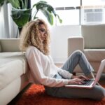 woman sitting on floor and leaning on couch using laptop